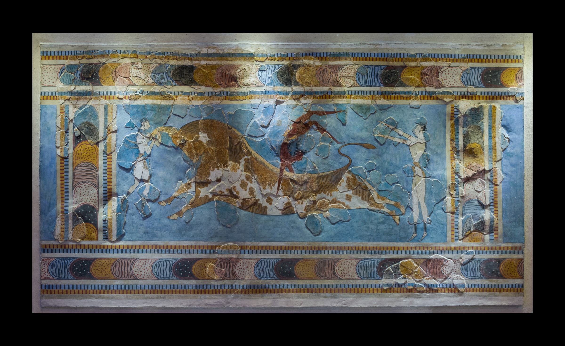 The Bull-Leaping (Toreador) Fresco from the Palace of Knossos, a reconstruction showing acrobats vaulting over a charging bull on a deep Aegean-blue ground, framed by banded borders of spirals and rosettes.
